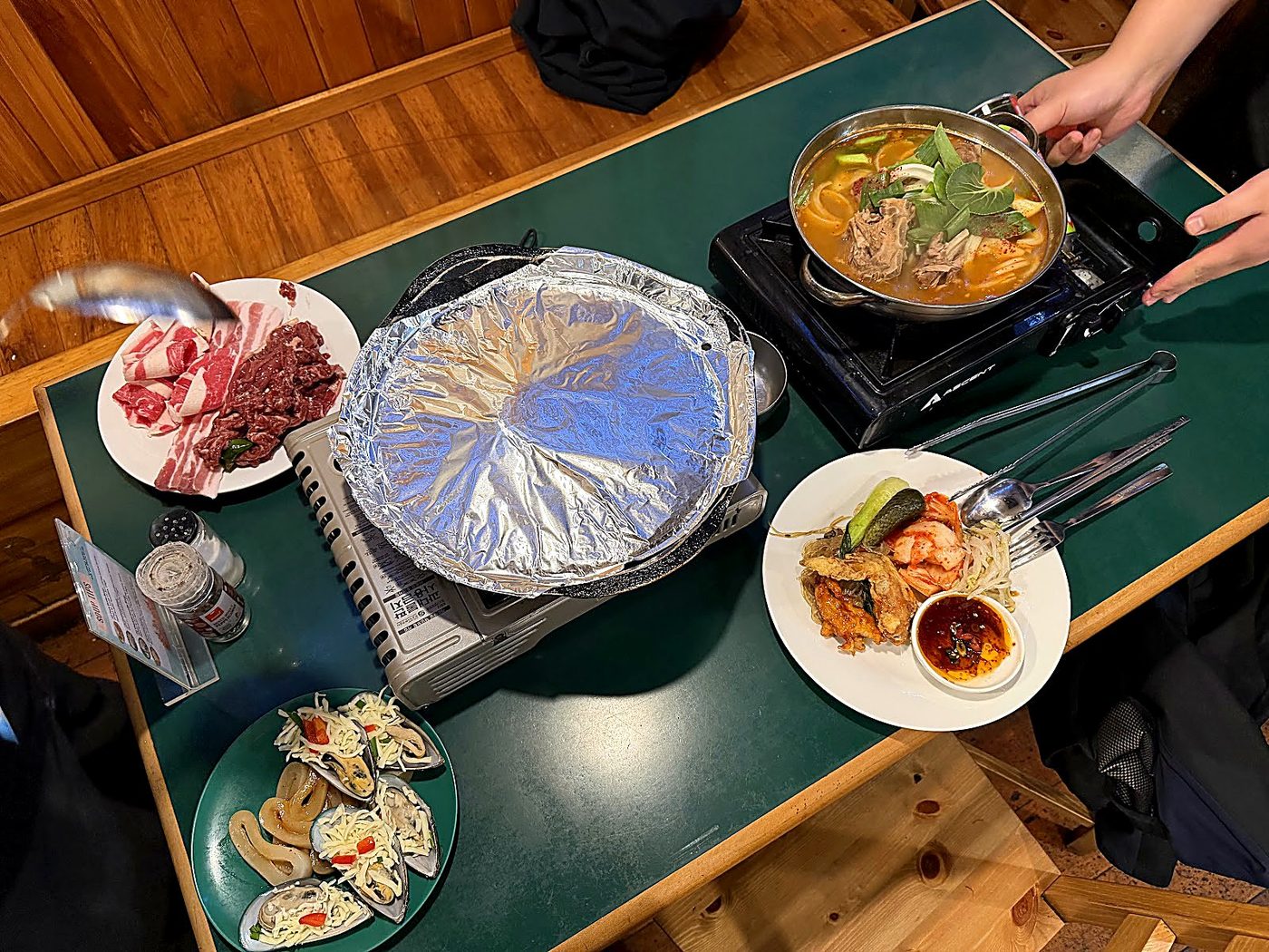 Tabletop cooking setup with foil BBQ dome and bubbling Korean soup hotpot